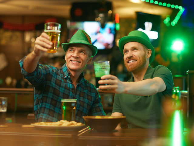 Two guys toasting pints of beer at a bar.