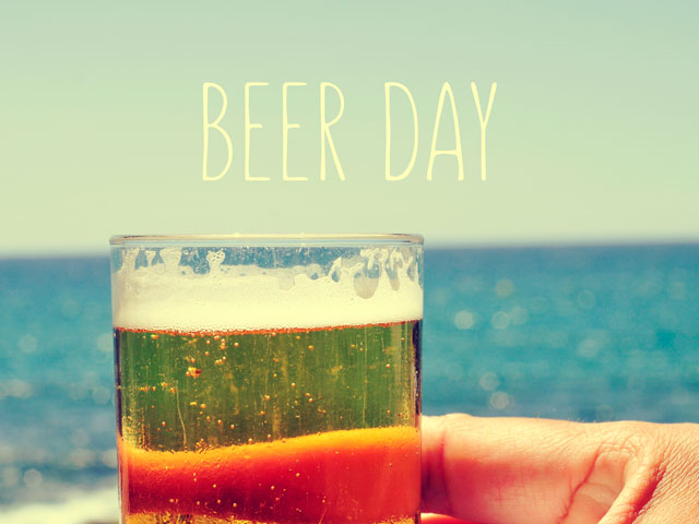 A person holding a beer celebrating National Beer Day on a beach