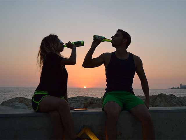 People chugging a bottle of beer at sunset near the beach