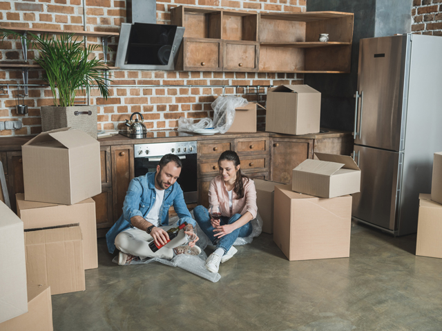 A couple unpacking bottles of wine out of boxes and drinking a glass