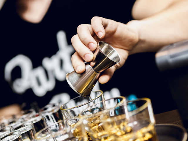 A bartender pouring shots from a jigger