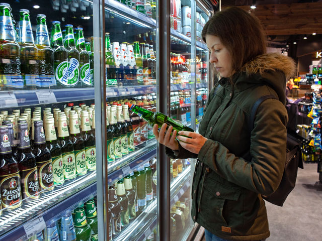 A woman in a beer store checks the expiration date of a bottle of beer