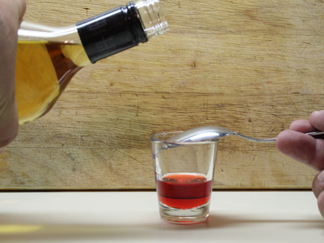 Pouring 1oz of 151 Rum into the shot glass and layering over grenadine